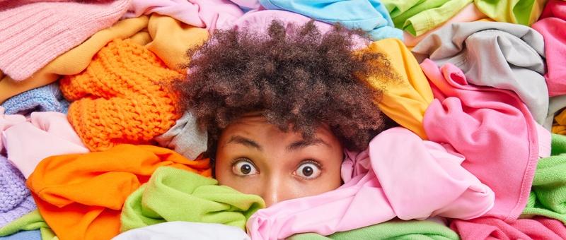 Surprised African American woman buried in brightly coloured laundry clothes.