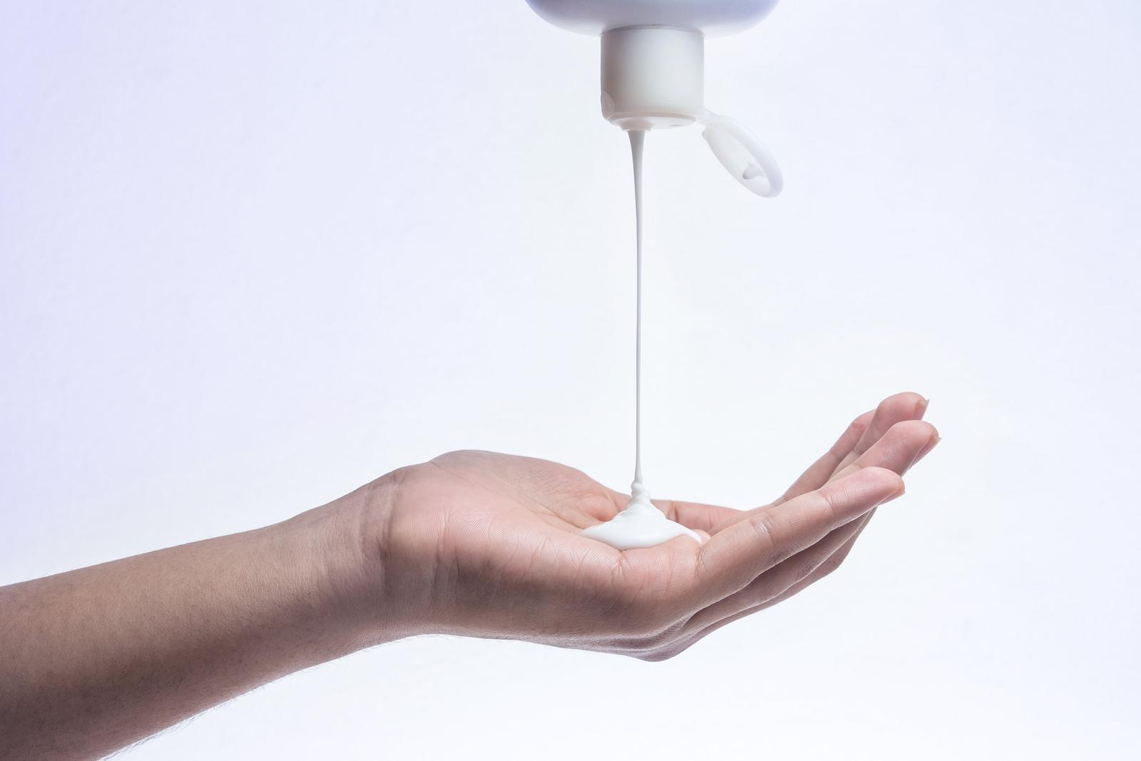 White liquid soap dispensing from a pump bottle onto an outstretched palm against a light background.
