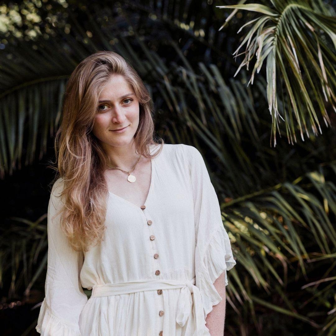 Helena Barham-Coppola, Nutritional Therapist, Nourish&Be, London, UK - woman in white dress with long, dark blonde hair against green, leafy nature background.