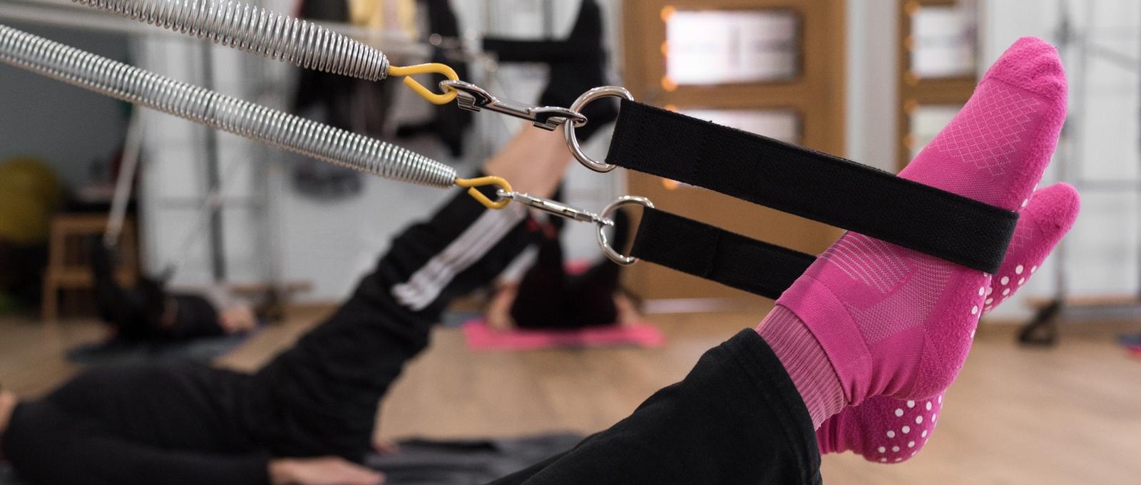Anonymous female in bright socks raising legs and stretching springs during group Pilates training in studio