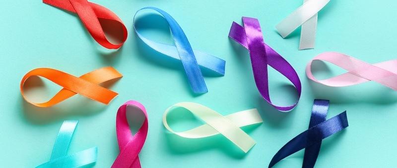 Multi-coloured cancer awareness ribbons against a vibrant pale blue background.