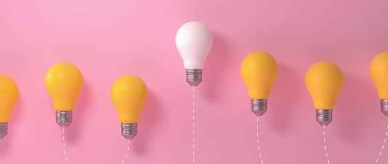 7 lightbulbs against pink background - six yellow, with one white floating above the rest.