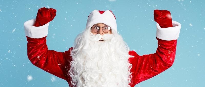 Red and white bearded Santa Claus wearing glasses with arms raised and fists clenched in a motivational stance against a snowy blue background.