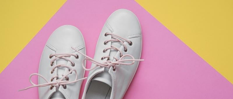 White plimsolls with pink laces against a geometric pink and yellow background.