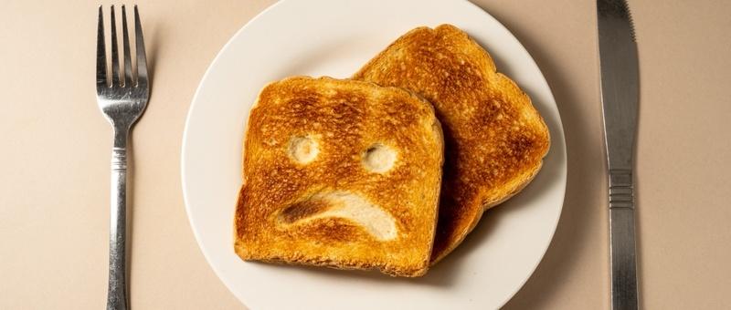 Two slices of golden-brown toast on a white plate with a sad face pattern, flanked by a fork and knife.