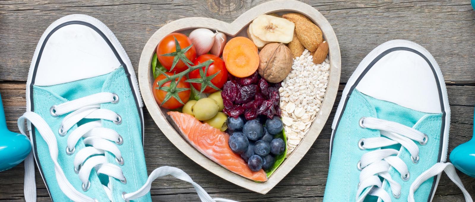 Healthy lifestyle concept with food in heart and sports fitness accessories on wooden boards.