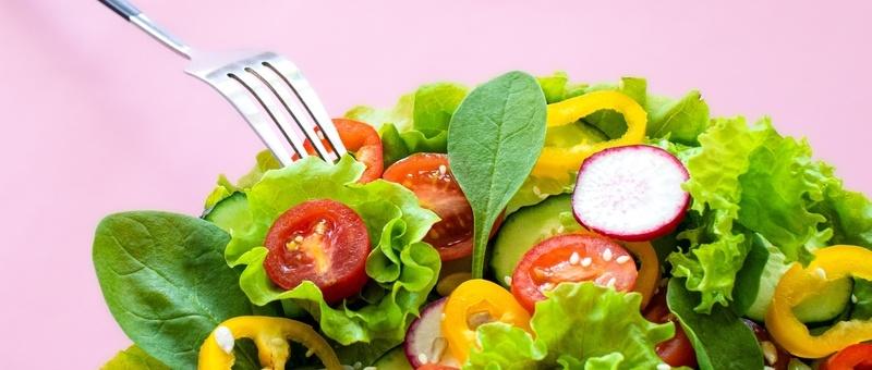 Colourful salad vegetables in a dish with fork against a pink background.