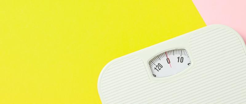 White weighing scales on two tone yellow and pink background.