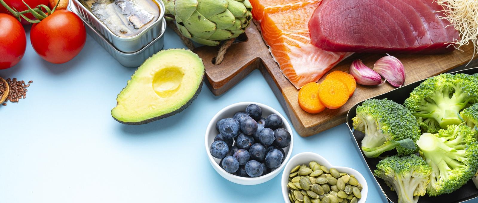 Foods to help with long-term inflammation such as fish, vegetables, nuts, seeds and fruit - all against blue background.