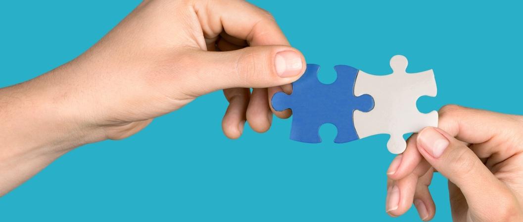 Human hands joining jigsaw puzzle parts on blue background.