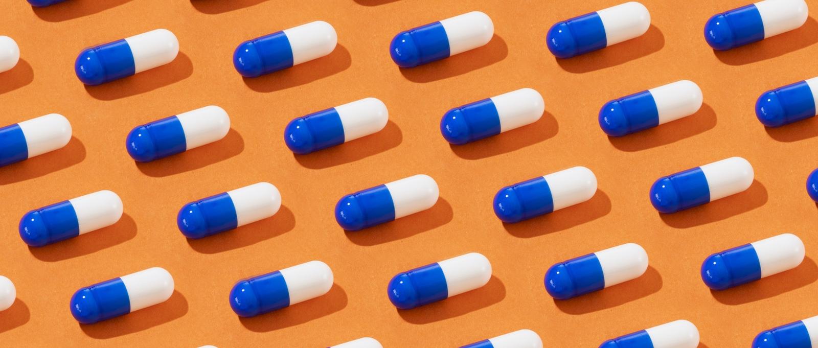 Blue and white capsule pills arranged in neat rows on an orange background, casting small shadows.