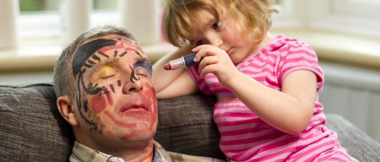 Little girl drawing on sleeping father's face