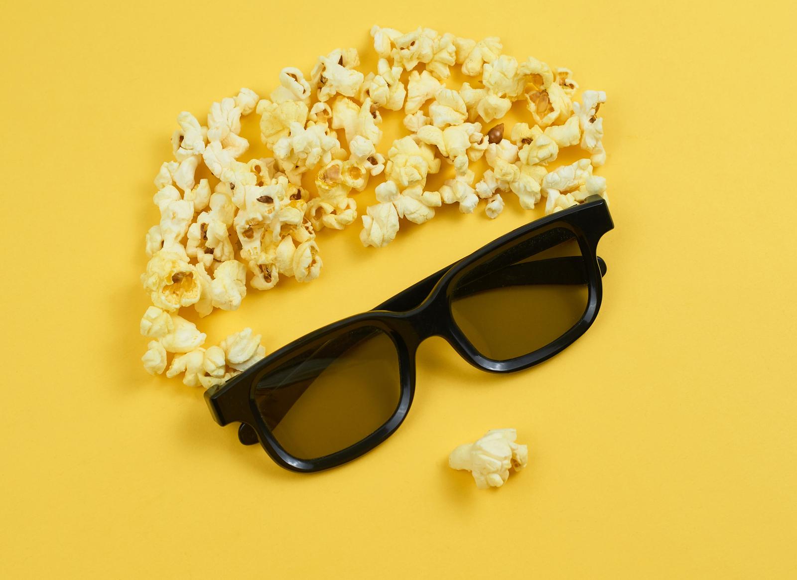 Black glasses with scattered popcorn in the form of a brain on a bright yellow background.