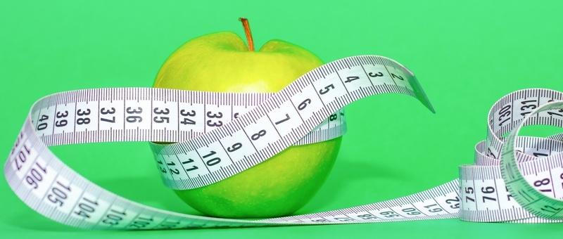 Green apple wrapped in measuring tape against green background.