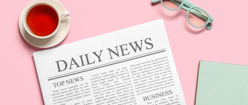 Newspaper with 'daily news' printed at top, surrounded by white cup and saucer filled with black tea, turquoise spectacles, and turquoise notebook, against pink background.
