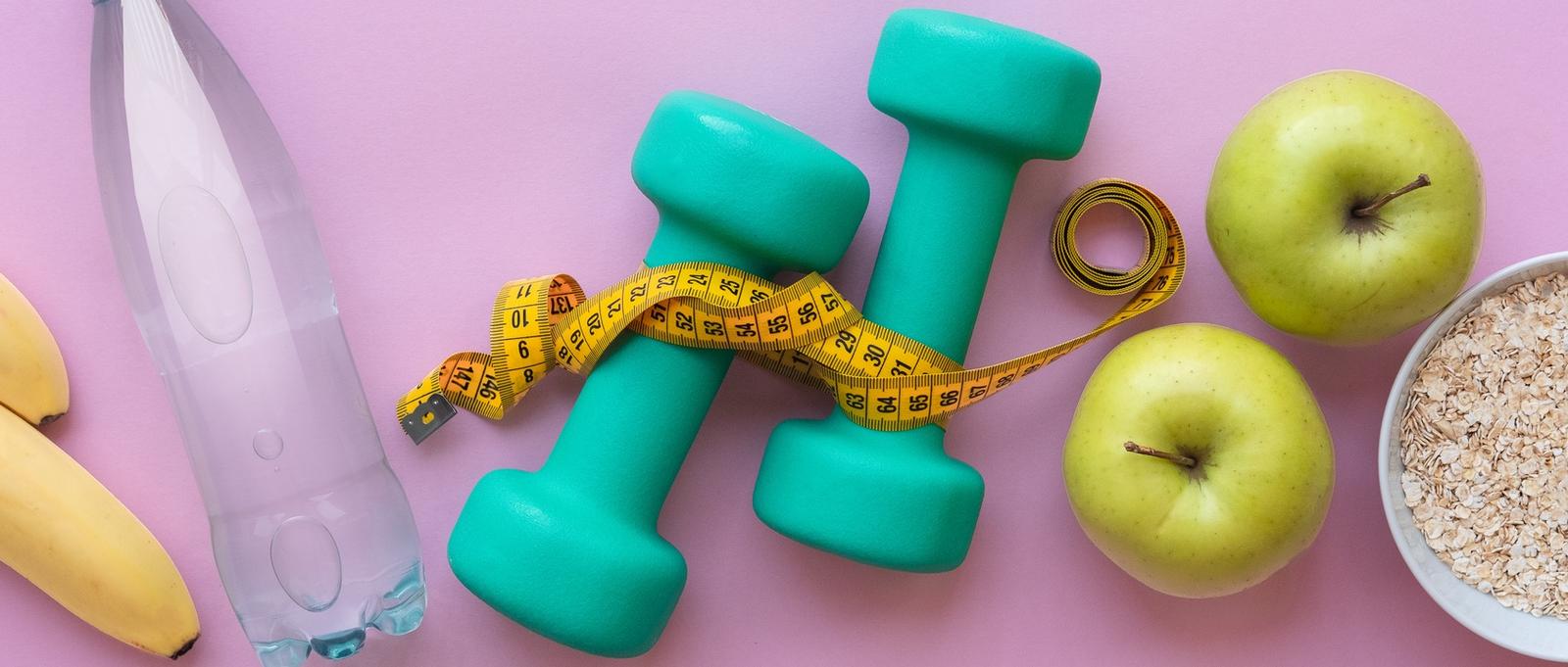 Fitness concept - apples, water, dumbbells and skipping rope on pink background