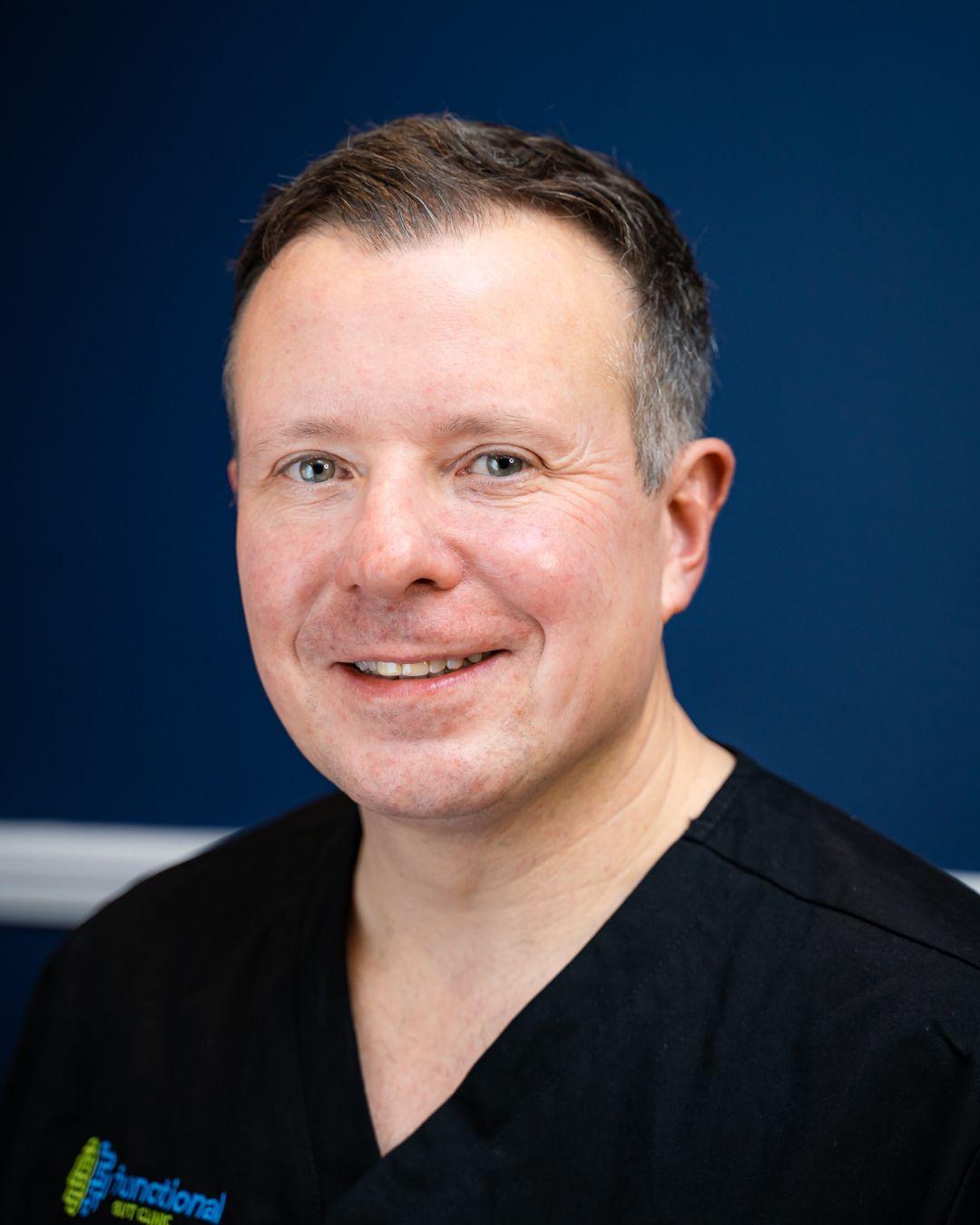 Professor Anthony Hobson of The Functional Gut Clinic, and host of The Functional Gut Diaries - white Caucasian male with short brown, grey hair in dark blue medical uniform against a dark blue background.
