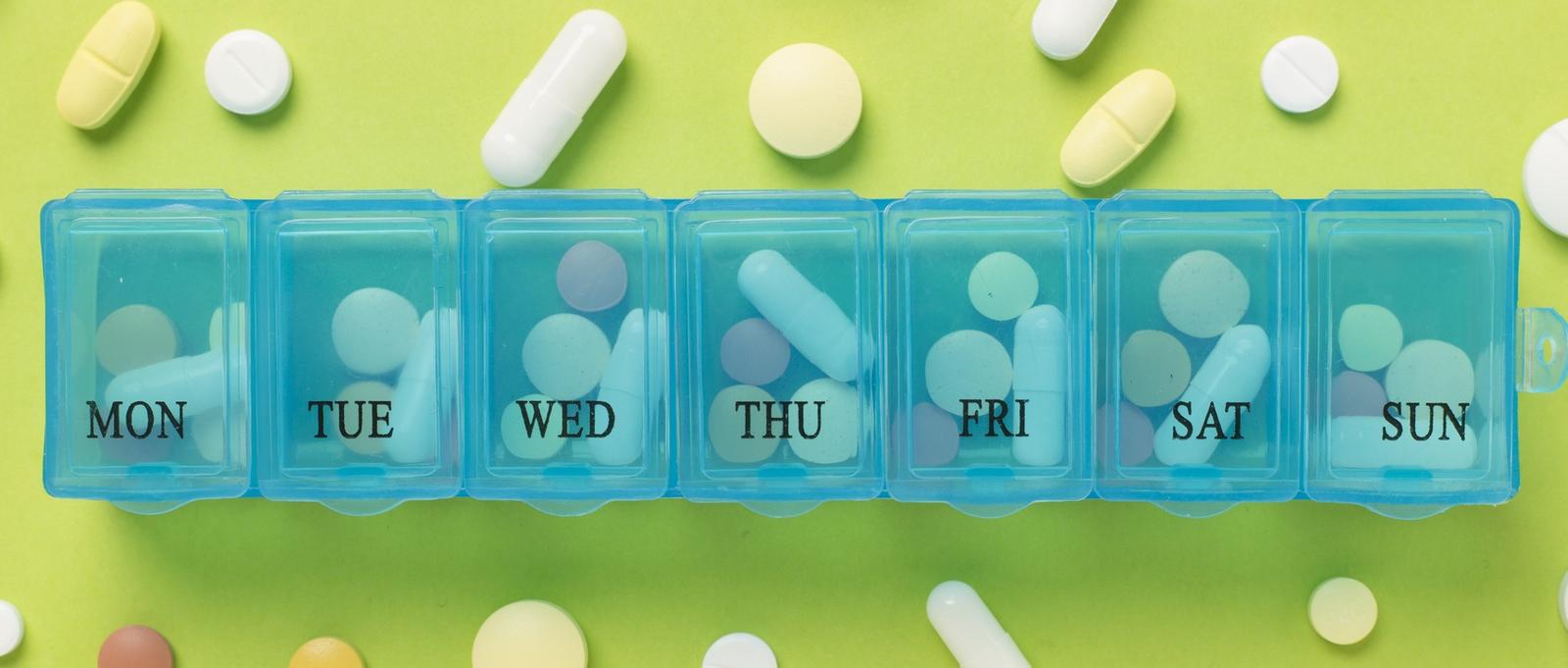 Pill organiser. Various capsules, vitamins and antibiotics in a plastic daily box. Green background.