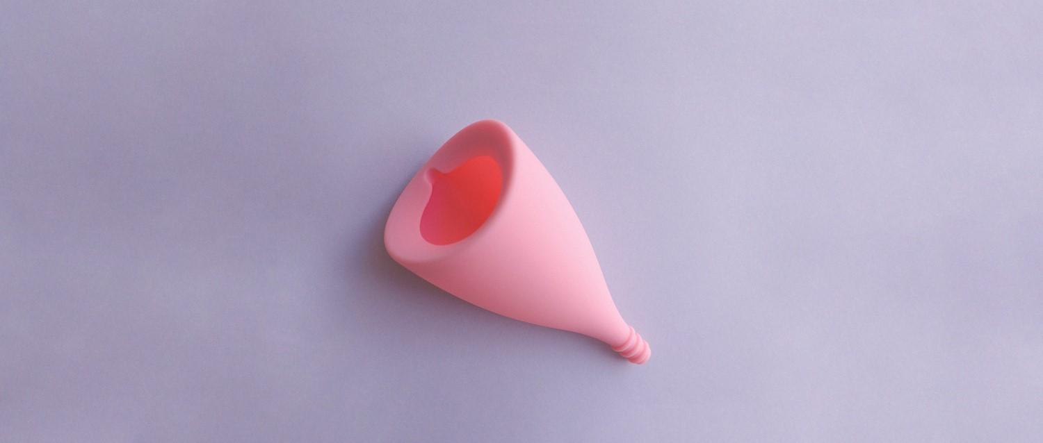 Pink menstrual cup lying on a light purple background, showing its cone shape and hollow interior.
