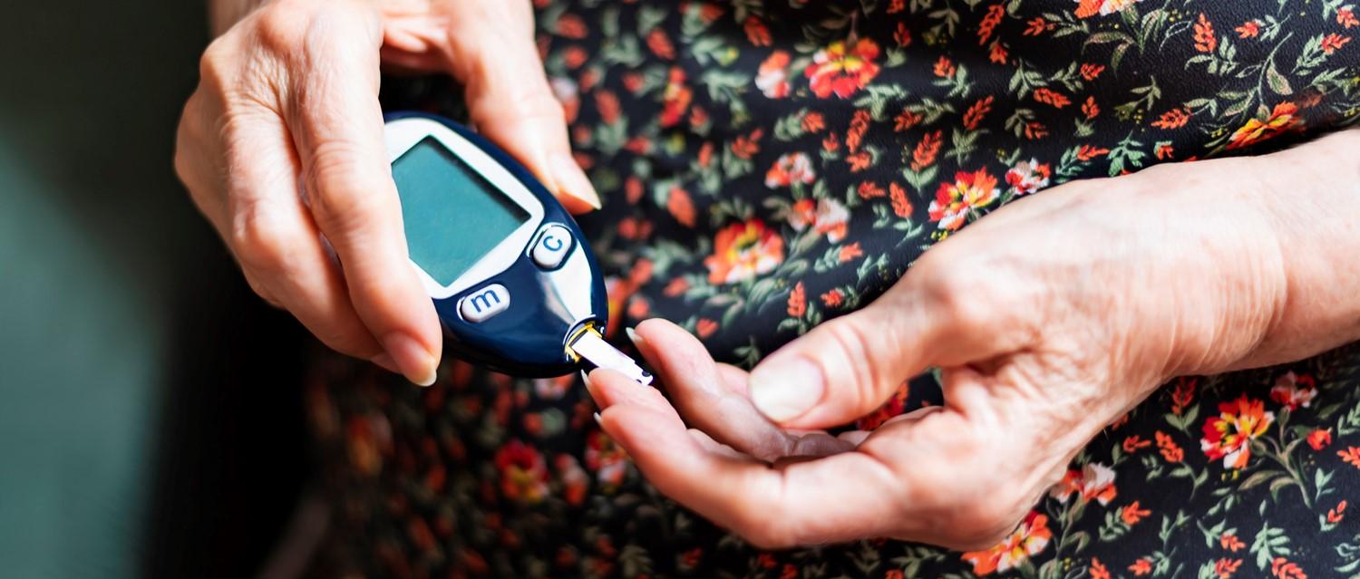 Person using a glucose monitor to test blood sugar, wearing a floral patterned dress.