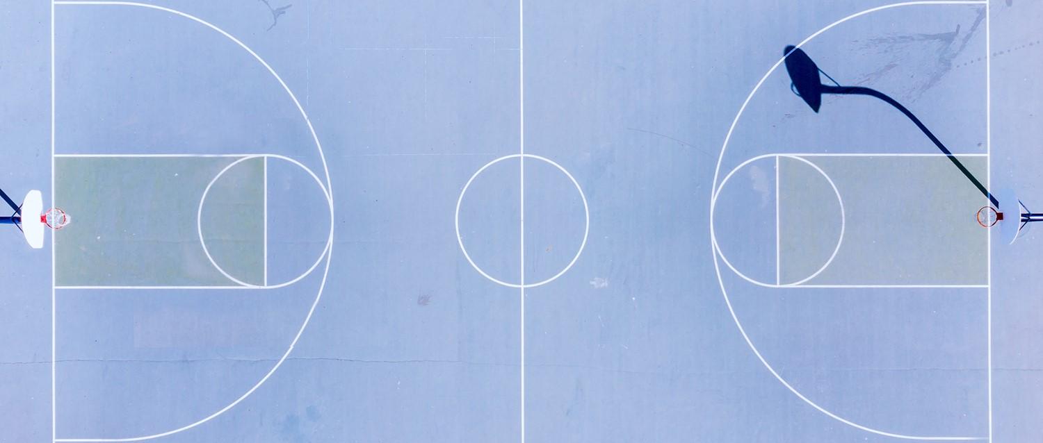 Aerial view of a blue basketball court with white line markings and hoops at either end, seen from directly above.
