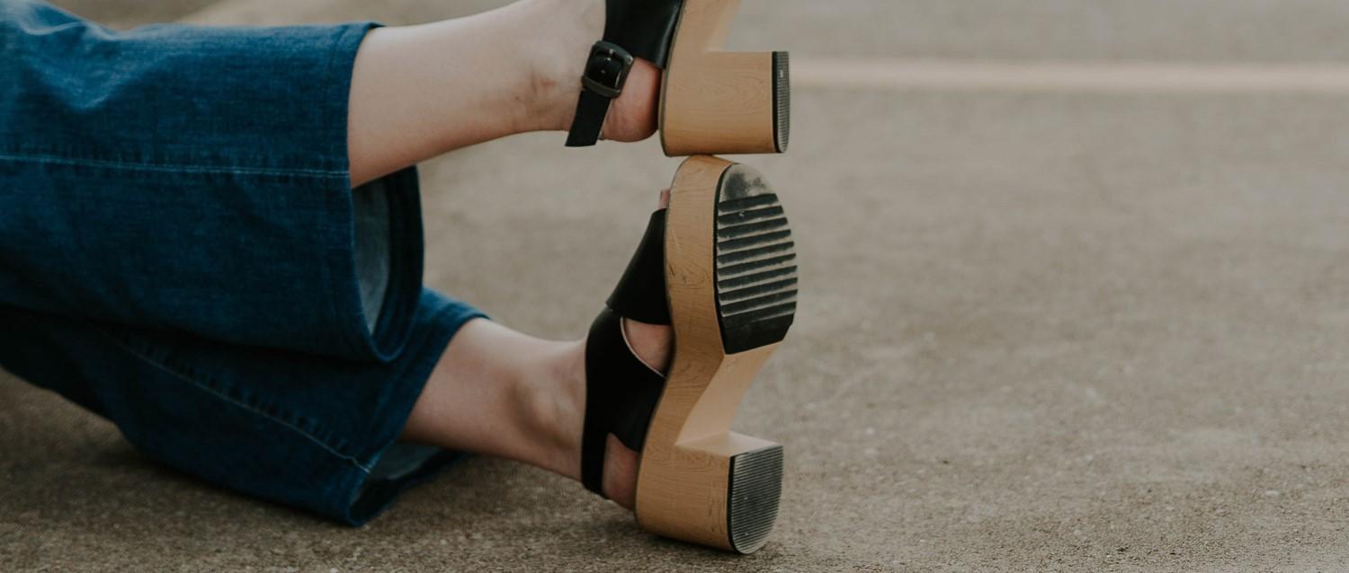 Person wearing blue jeans and black sandals with wooden heels with lipodema, with a black watch on their wrist.
