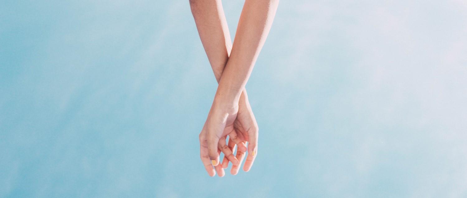 Two hands gently touching with fingers intertwined against a light blue background, conveying intimacy and connection.