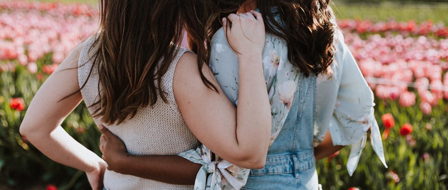 Two people embracing in a field of pink tulips Supporting a friend with baby loss, wearing light summer clothing with floral patterns.